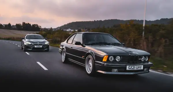 Klasyczne bmw 635 csi i nowszy model jadą drogą o zachodzie słońca.