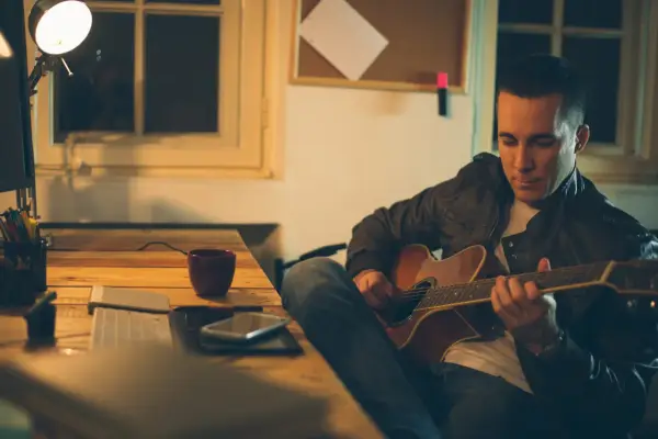Mężczyzna gra na gitarze, ćwicząc skale gitarowe przy biurku.