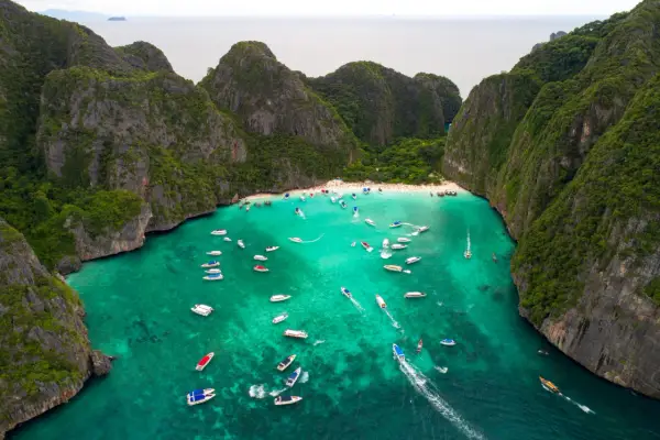 Maya Bay tętni życiem, pełna łodzi i turystów na piaszczystej plaży, otoczona stromymi, porośniętymi zielenią klifami.