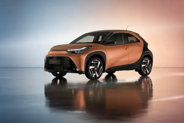 Pomarańczowy Toyota Aygo Cross z czarnymi akcentami i stylowymi felgami, odbijający się w lustrzanej podłodze.