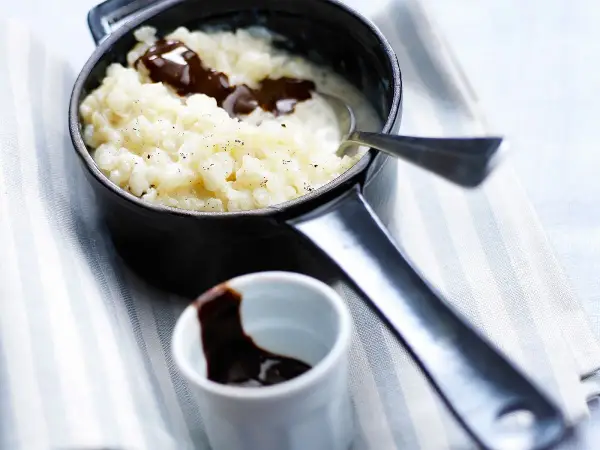 Un délicieux riz au lait au chocolat, servi dans une petite casserole noire, avec une cuillère et un ramequin de sauce chocolat.