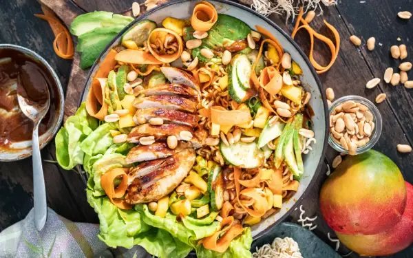 Ein bunter asiatischer Salat mit gegrilltem Hähnchen, Avocado, Mango, Karottenstreifen und Erdnüssen.