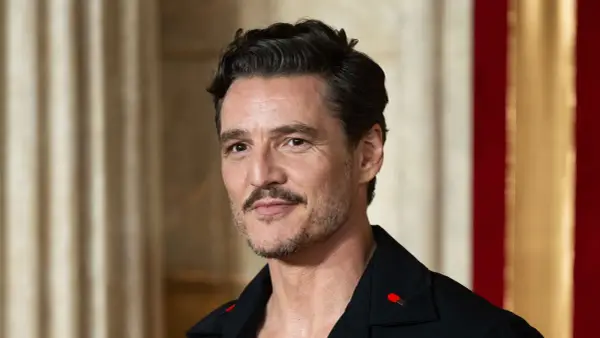 Pedro Pascal con cortes de pelo hombre corto por los lados y largo arriba, luciendo un pin de cerilla en su solapa.