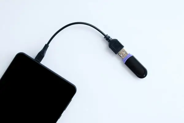 Czarny pendrive podłączony do telefonu przez kabel. Tak, można podłączyć pendrive do telefonu, by przenieść dane.