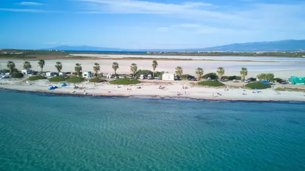 Spiaggia di Putzu Idu con palme, camper e gente che si gode il sole. Acqua cristallina e cielo azzurro.