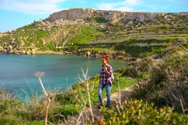 Malta w marcu: kobieta na ścieżce z widokiem na turkusową zatokę i zielone wzgórza. Pogoda idealna na spacer.