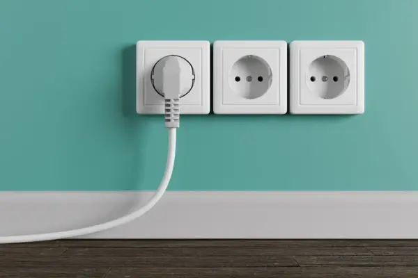 Tres enchufes blancos en una pared turquesa, uno con un enchufe gris conectado. La altura de los enchufes en la cocina es estándar.