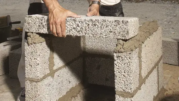 Byggare lägger mura lecablock på betongplatta. Murbruket syns mellan blocken.