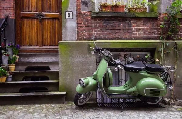 Zielony skuter, klasyk, czeka na właściciela. Parkowanie motocykla na chodniku przed drzwiami z numerem 9.