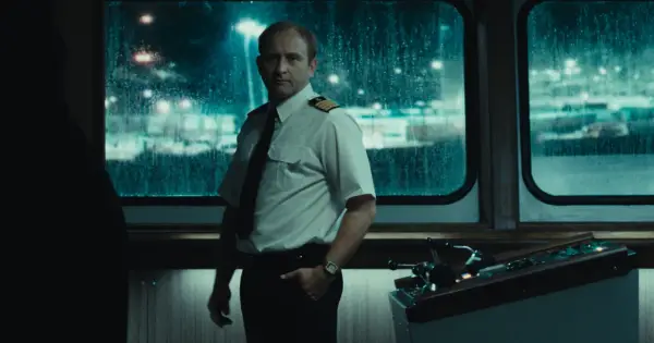 Kapitan w białej koszuli i krawacie stoi przy sterach statku. Scena z jednego z filmów Jana Holoubka.