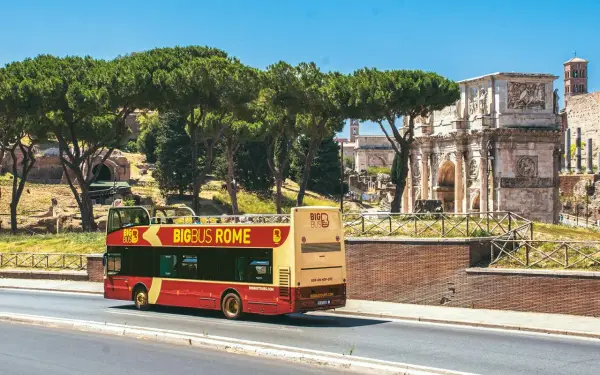 Un bus touristique rouge et jaune circule près de l'Arc de Constantin. Le Vatican n'est pas loin, offrant une vue sur Rome.