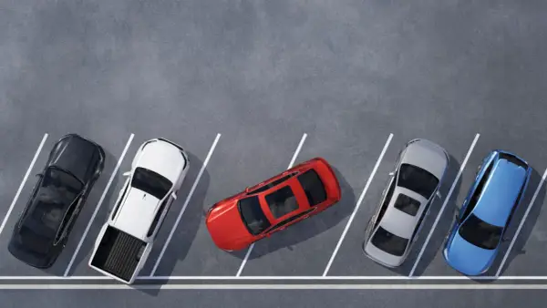 Czerwony samochód zajmuje dwa miejsca parkingowe, blokując sąsiednie pojazdy. Obok stoją czarny, biały pickup, srebrny i niebieski.