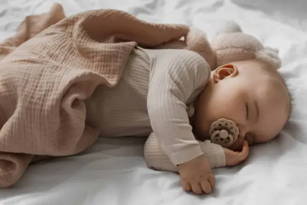 Dolce neonato di 3 mesi dorme sereno, avvolto in una copertina rosa cipria, con un ciuccio in bocca.