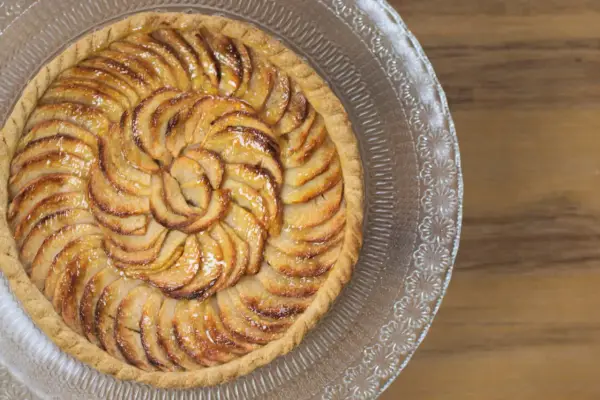Tarte aux pommes dorée sur pâte feuilletée, disposée en spirale sur un plat en verre gravé. Un délice croustillant.