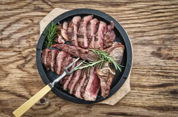 Una succulenta bistecca fiorentina affettata, guarnita con rosmarino, pronta per essere gustata.