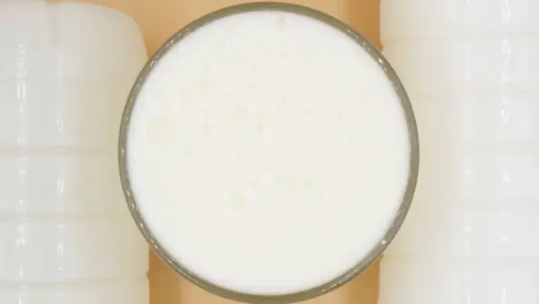 Szklanka pełna pianistego kefiru, otoczona białymi butelkami. Idealny moment, kiedy pić kefir, to teraz!