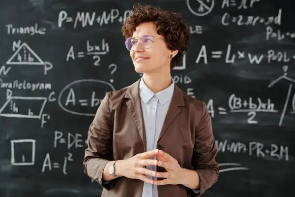 Lehrerin vor Tafel mit Matheformeln. Sie fragt sich, wie viel verdienen Grundschullehrer.
