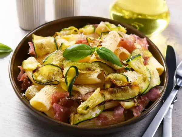 Makaron z cukinią i szynką parmeńską, ozdobiony bazylią. Idealne szybkie dania z cukinią na obiad.