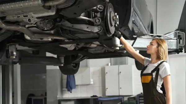 Mechaniczka sprawdza układ napędowy samochodu na podnośniku.
