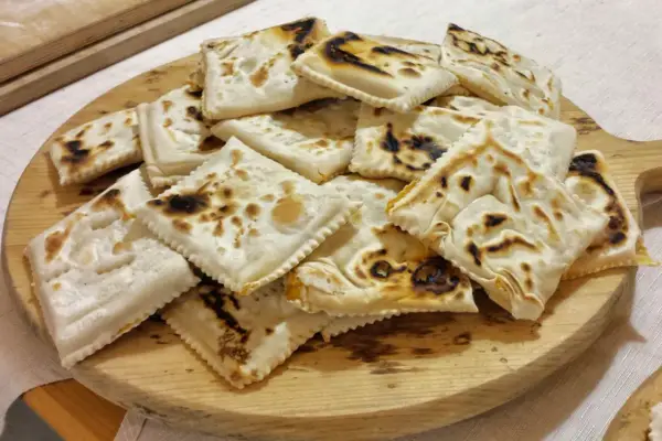 Piatto tipico cesenate: piadina fritta, dorata e leggermente bruciacchiata, servita su un tagliere di legno.