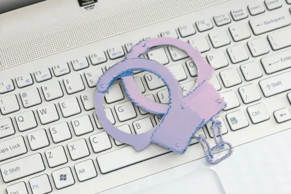 Różowe kajdanki leżą na białej klawiaturze laptopa.