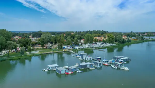 Nowoczesne houseboat'y unoszą się na spokojnej wodzie, obok kempingu z kamperami.