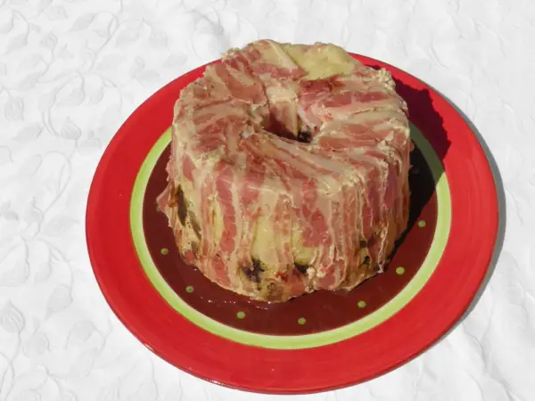 Un pâté en croûte de lard, une recette qui ne demande pas de farcement. Il est servi sur une assiette rouge décorée.