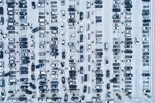 Zimowy parking z wieloma samochodami. Wygląda, jakby druga rata OC po terminie, bo tyle aut stoi w śniegu.