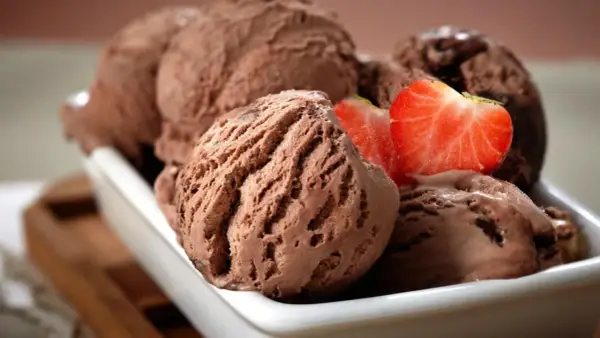 Cucharadas de cremoso helado de chocolate, decoradas con fresas frescas, listas para disfrutar.