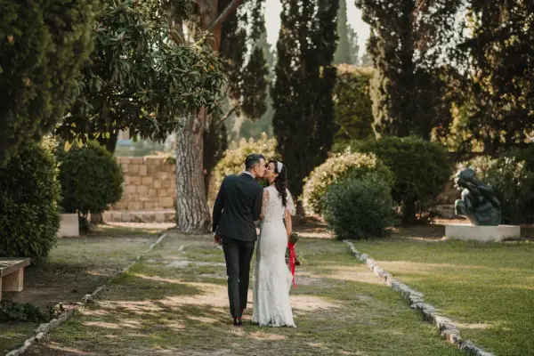 Ein Brautpaar küsst sich im Park. Die Braut trägt ein Spitzenkleid, der Bräutigam einen dunklen Anzug. Eine kroatische Hochzeit im Grünen.