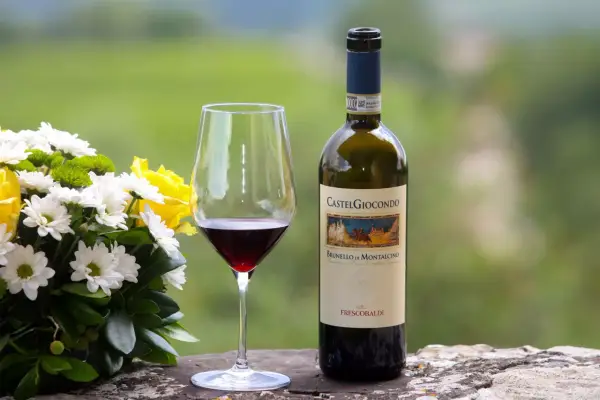 Un bicchiere di Brunello di Montalcino, un vino pregiato, accanto a un bouquet di fiori e una bottiglia CastelGiocondo.