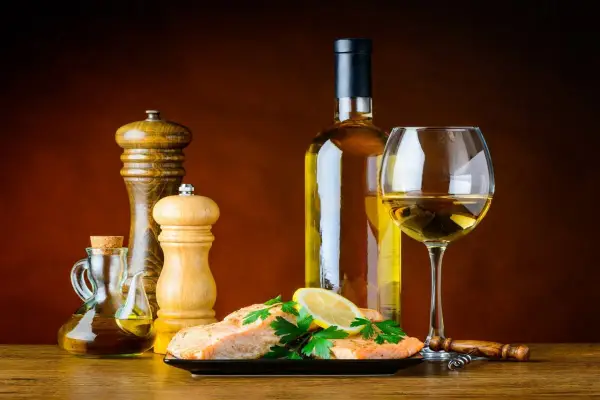 Un plat de saumon avec citron et persil, accompagné d'une bouteille et d'un verre de bon vin blanc sec, d'une salière, d'une poivrière et d'une burette d'huile d'olive.
