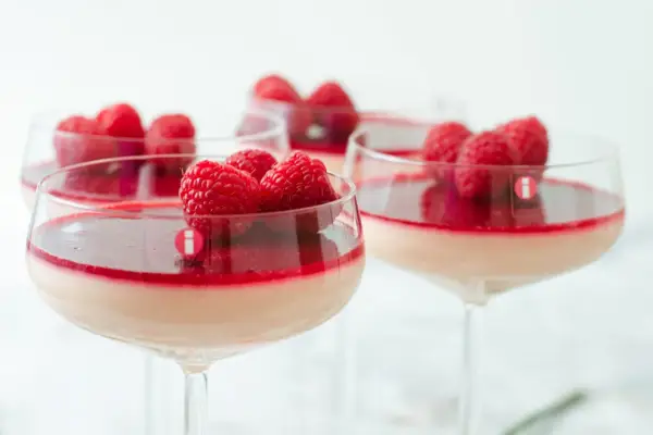 Flera glas med krämig pannacotta, toppad med hallon och en röd sås. En perfekt dessert i glas.