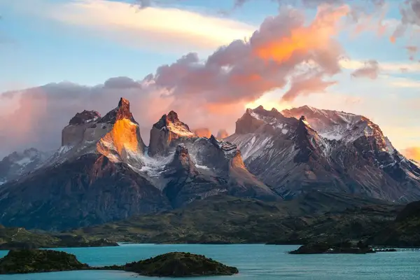 Wspaniała wycieczka do Chile! Słońce oświetla skaliste szczyty Torres del Paine, odbijając się w turkusowym jeziorze.