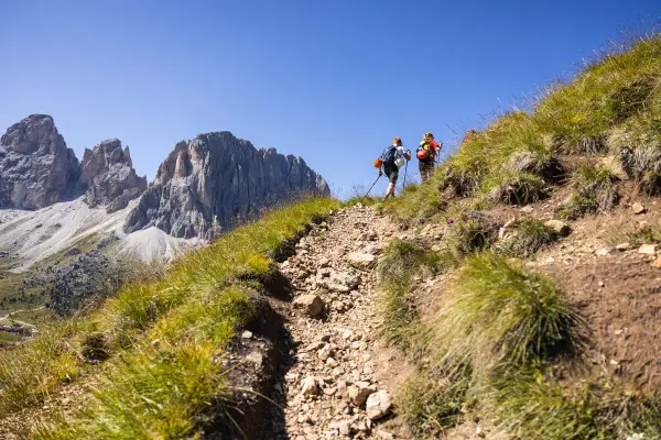 Due escursionisti affrontano un sentiero roccioso sui **cammini in Trentino**, con imponenti vette sullo sfondo.