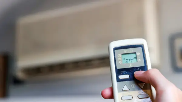 Mano ajustando el control remoto de un aire acondicionado cool o heat. La pantalla muestra 27°C.