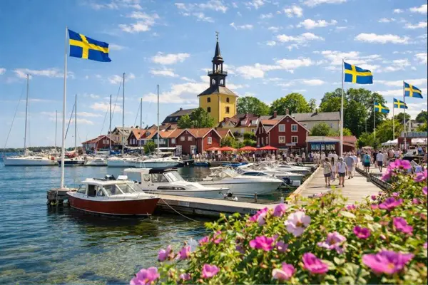En livlig hamn med svenska flaggor, båtar och röda hus. Kanske en vy från ett mysigt hotell i Norrbotten en solig sommardag.