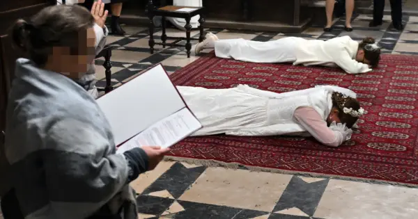 Dwie kobiety w białych sukniach leżą na dywanie w kościele. To uroczystość, podczas której zostają dziewicami konsekrowanymi.