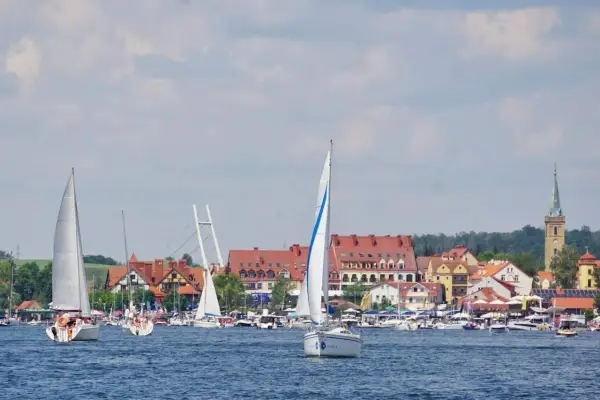 Żaglówki na jeziorze przed malowniczymi mazury miasta z czerwonymi dachami i wieżą kościelną.