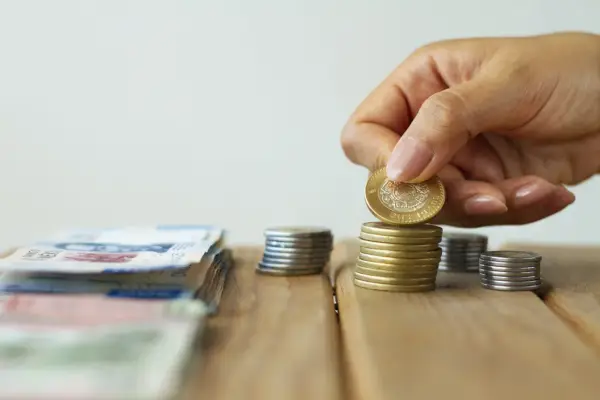 Dłoń kładzie monetę na stosie, obok leżą banknoty. To symboliczne przedstawienie oszczędności i potencjalnych korzyści z ulgi podatkowej do 26 lat.