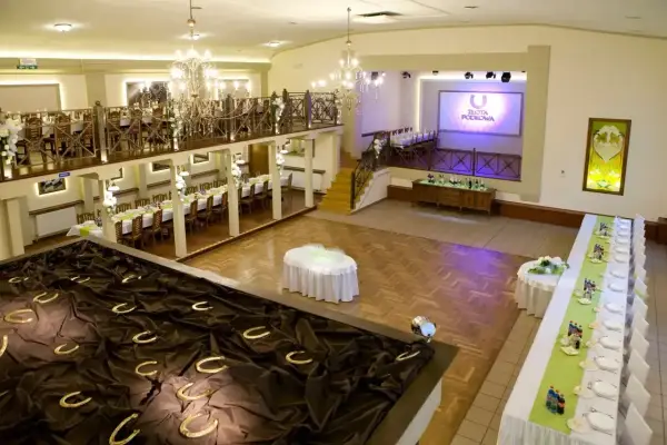 Elegancka sala weselna z podkowami na ciemnym materiale, stołami i ekranem z logo "Złota Podkowa".