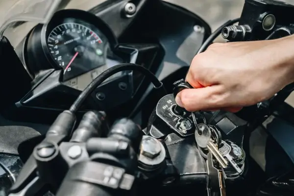 Mano girando la llave de contacto de una moto, pero no enciende. El tablero y las llaves están visibles.