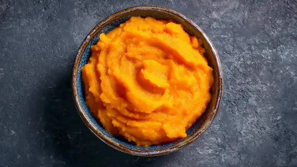 Un cuenco de cremoso puré de boniato, con su vibrante color naranja, listo para ser disfrutado.