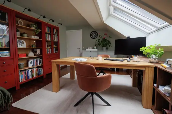 Accogliente angolo studio in mansarda con scrivania in legno, librerie rosse e lucernario.