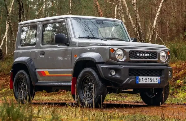 Szary Suzuki Jimny 2026 z kolorowymi pasami na boku, gotowy na terenową przygodę w lesie.