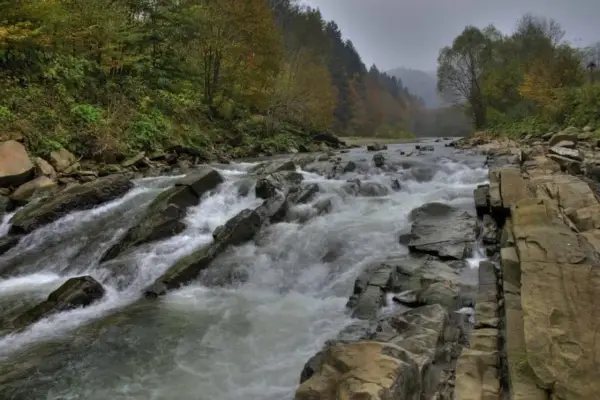 Kamieniste koryto rzeki w Bieszczadach, gdzie rwący nurt pokonuje skalne progi. W tle jesienne drzewa.