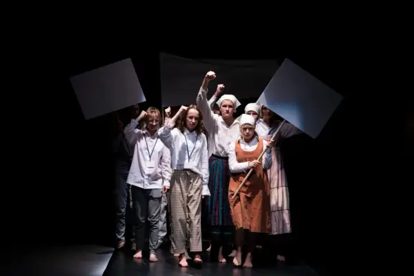 Młoda grupa teatralna z transparentami wznosi pięści. Występ na czarnym tle.