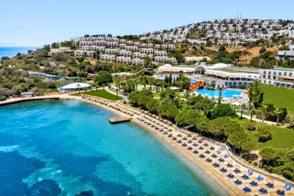 Widok na hotel Yasmin Bodrum Resort z plażą, basenami i białymi budynkami na wzgórzu. Idealne miejsce na wakacje, jak sugerują yasmin bodrum resort opinie.