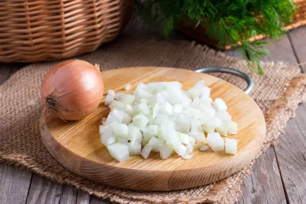 Cipolla intera e tritata su tagliere di legno. Un rimedio naturale per come togliere l'odore di aglio dalla bocca.