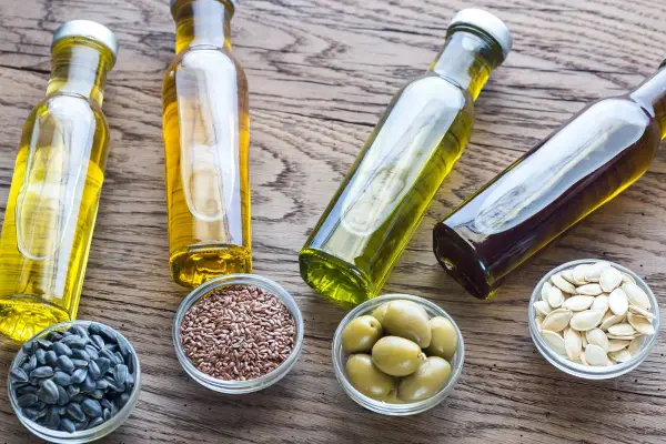 Bouteilles d'huile de cuisson dorée et ambrée, avec des graines de tournesol, de lin, des olives et des pépins de courge.